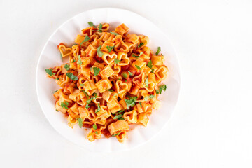 Heart shaped pasta with tomato sauce. Classic italian marinara or bolognese pasta with fresh herbs, simple and delicious recipe for Valentine day or date night, on white table copy space