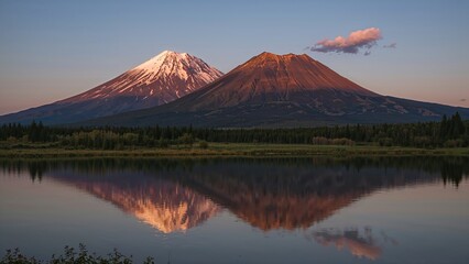 Two mountains with snow-capped peaks reflected in a lake during sunset or sunrise.