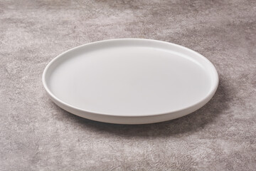 empty matte white ceramic plate with round rim on textured grey concrete stone background surface, rustic dining or menu concept with copy space