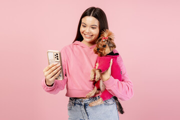 Woman and Yorkshire terrier dog taking a selfie together on pink background