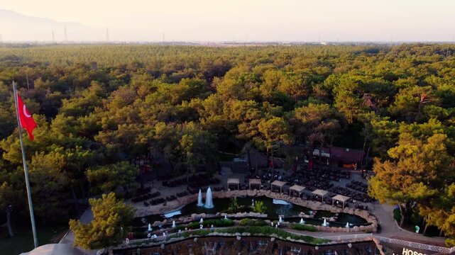 Aerial drone flyaway from Atat&uuml;rk head monument in Antalya at sunset. Waterfall flowing from cliff surrounded by green park and forest. 