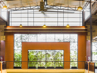 Industrial interior with exposed steel trusses, brick wall detailing, and large grid windows framing lush greenery. Clean lines, warm lighting, and a balanced architectural composition.