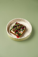 Flavorful open-faced sandwich features layers of savory toppings including fish, herbs, and a drizzle of sauce, set on a textured plate, bringing a touch of art to the dining table