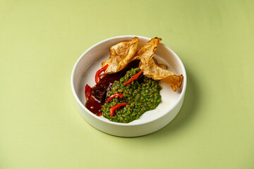 A plate presents a vibrant green sauce garnished with red chili slices, paired with crispy snacks and a rich, dark red dip. The setting is lively and inviting