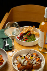 Colorful plates filled with gourmet food are elegantly arranged on a wooden table. A glass of white wine complements the vibrant meal, creating a delightful dining atmosphere