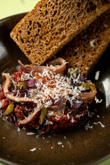 A delicious meal features marinated fish along with vibrant vegetables, topped with shredded cheese. Rustic brown bread rests beside this culinary creation in an inviting setting