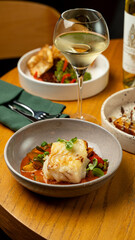 Delicate fish rests on a colorful bed of sautéed vegetables, harmonized by a glass of refreshing white wine nearby, inviting a delightful culinary experience