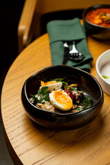 A cozy café table features a colorful salad bowl, garnished with fresh vegetables and a perfectly cooked egg. The warm atmosphere invites diners to enjoy a peaceful lunchtime experience