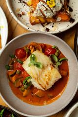 A beautifully plated fish with a crispy crust sits atop a colorful mix of vegetables and sauce, showcasing a delightful culinary creation perfect for an evening meal with friends