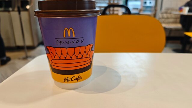 Takeaway coffee cup with colorful Friends themed design placed on a table inside a modern fast food cafe in Kyiv, Ukraine, 11.12.2025. The image represents branded lifestyle, pop culture