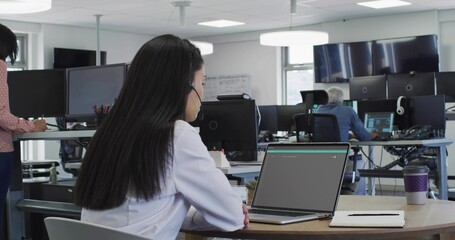 Obraz premium Typing headset-wearing woman in white blouse using laptop at open office table, copy space