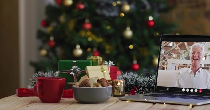 Chatting senior woman on laptop in white shirt, waving at holiday home with cookies, copy space - Powered by Adobe
