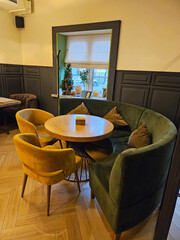 Green couch with four yellow chairs around it. The chairs are facing a table near window