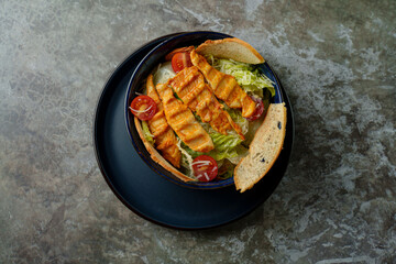 An appetizing bowl showcases vibrant greens topped with perfectly grilled salmon and cherry tomatoes, accompanied by a slice of crusty bread on a textured surface
