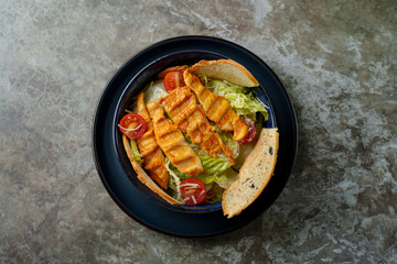 Freshly grilled chicken strips rest atop a bed of crisp lettuce and vibrant cherry tomatoes, all served in a warm bread bowl at a charming cafe. Lunchtime joy fills the air