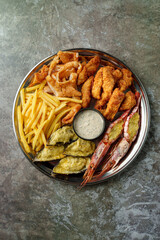 A delectable seafood platter filled with golden fried shrimp, crispy fish fillets, and crunchy fries, accompanied by a rich dipping sauce, perfect for sharing at a cozy restaurant