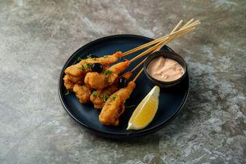 Delight in a plate of golden fried shrimp skewers, perfectly crispy and garnished with herbs, served alongside a tangy sauce and a wedge of lemon for extra flavor