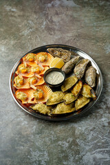 An enticing seafood platter features beautifully arranged shrimp, oysters, and scallops, served with a lemon wedge and tangy sauce for dipping, perfect for sharing