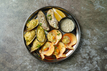 A vibrant platter showcases baked oysters and scallops, garnished with herbs, served alongside creamy sauce and a fresh lemon wedge, inviting seafood lovers to indulge