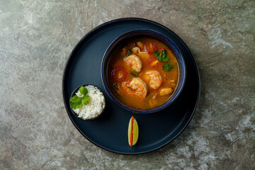A delicious bowl of shrimp stew simmers with vibrant vegetables, accompanied by fluffy rice and a slice of lime for a refreshing touch