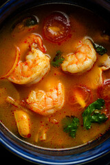 A cozy kitchen scene features a bowl of shrimp soup gently simmering. Juicy shrimp float alongside ripe tomatoes and fresh herbs, creating a warm and inviting aroma