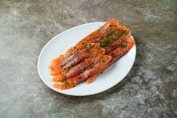 Vibrant salmon fillets lie on a smooth white plate, enhanced with a sprinkle of fresh herbs. This dish showcases the beauty of fresh ingredients and culinary artistry