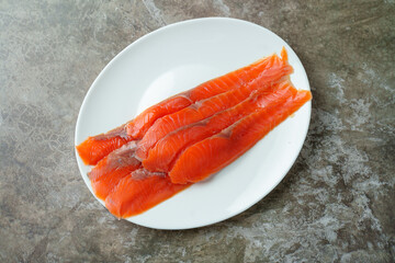 Bright orange salmon fillets lay artfully on a round white plate, showcasing their vibrant color