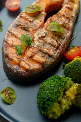 Savory grilled salmon takes center stage on a plate, accompanied by vibrant broccoli and cherry tomatoes. Fresh herbs add a burst of flavor, making for a wholesome dining experience