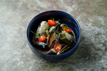 A vibrant bowl of fresh mussels is served in a rich creamy sauce, beautifully complemented by juicy cherry tomatoes and a sprinkle of fresh herbs, creating a colorful dish