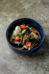 Fresh mussels cooked in a rich, creamy sauce, garnished with vibrant cherry tomatoes and herbs, elegantly displayed in a deep blue bowl on a textured surface