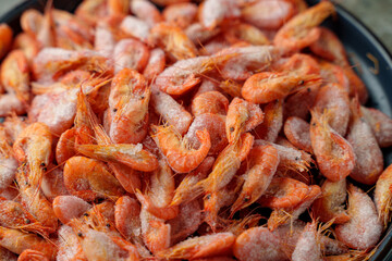 A vibrant scene reveals a large pile of shiny, frozen shrimp at a lively coastal market. Vendors and locals mix as the salty air fills with excitement and delicious aromas