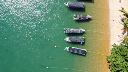 Drone image of beach with anchored boats, fishing village, forest, and construction site near shore. © Na'im
