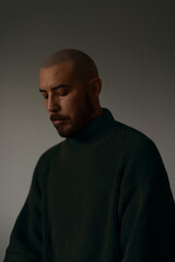 A man in a dark, textured turtleneck sweater is softly lit against a neutral background, creating a calm and introspective portrait. The warm tones and gentle shadows emphasize mood and simplicity.