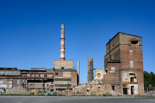 An abandoned factory with pipes, dilapidated brick buildings and pieces of walls under a clear blue sky
