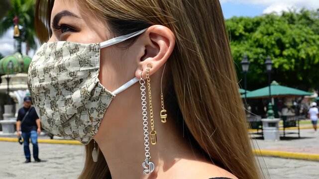 Young woman wears a mask and unique earrings in outdoor square during bright day