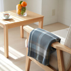 Cozy wooden armchair with plaid scarf and tea on table in bright sunlight - Scandinavian minimalist interior