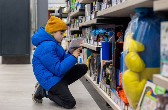 young boy shopping independently in a supermarket toy aisle, carefully choosing a toy from a store shelf. child independence, consumer choice, modern retail experience, education through play. Copyspa