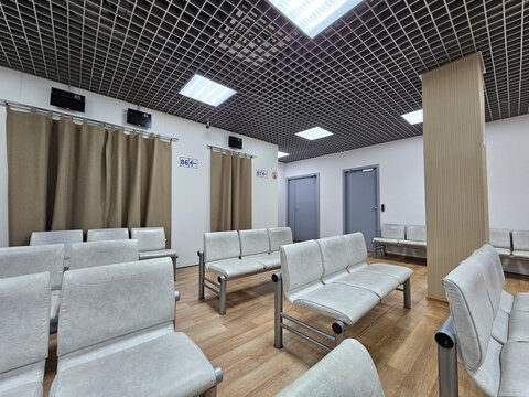 Large room with many chairs and a TV. The chairs are white and the room is mostly empty. curtains in the visa center. embassy of the country for tourist interior