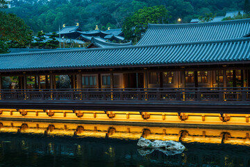 Hong Kong, Diamond Hill, China : illuminated temple corridor reflected on still water at blue hour inside Nan Lian Garden creating a serene urban night atmosphere