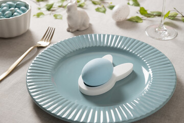 Close up of pastel blue Easter egg on bunny shaped holder placed on ceramic plate. Elegant spring table decor with soft light and minimal festive styling.
