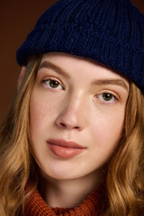 Charming redhead woman in cozy winter sweater posing against warm brown backdrop