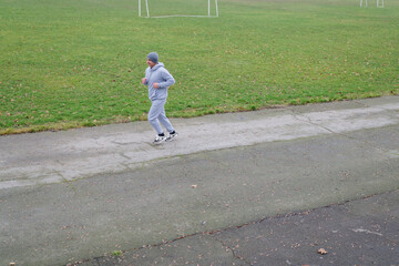 A person jogs along a path in a park on a cloudy morning. Grass and soccer goals are in the...