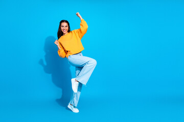 Young woman in yellow sweater dancing against blue background creating a fun stylish lifestyle and shopping vibe