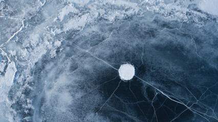 An overhead perspective of a frozen lake, with a bright circular opening visible in the center, surrounded by intricate ice formations and cracks