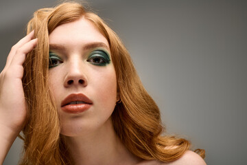 Stunning redhead model showcases bold eye makeup in a modern grey studio setting