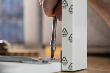 A human hand expertly uses a screwdriver to fasten a small screw into a white furniture panel, embodying efficient home assembly and practical DIY projects