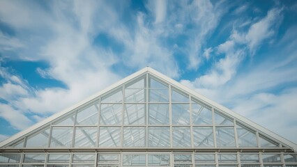 A modern glass building with a triangular roof under a partly cloudy sky.