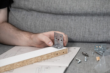 Man's hands assembling flat-pack furniture, attaching metal bracket to particle board piece, carefully following instruction manual for home DIY project