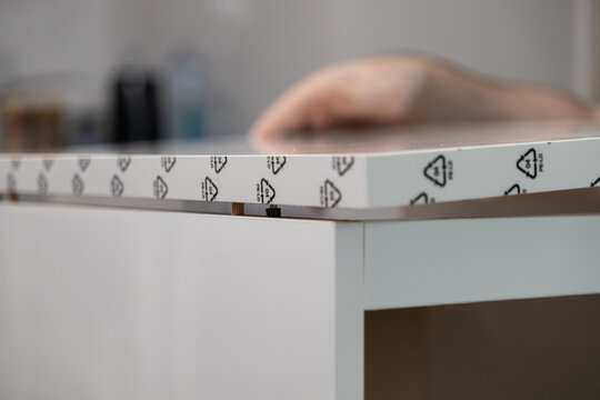Assembling white furniture panel reveals 04 PE-LD recycling symbol, dowels, and cam lock, emphasizing responsible material choice for sustainable home improvement