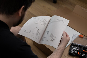 Young adult carefully reading detailed furniture assembly guide for a new purchase, focused on successful DIY home improvement project setup